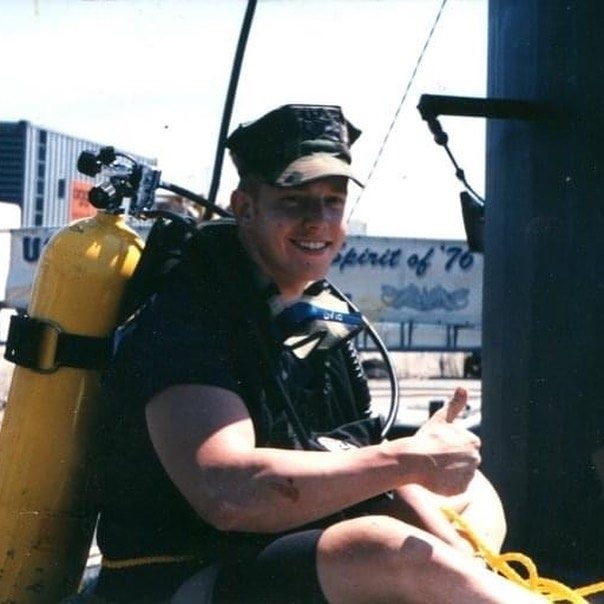 Young Jake in dive gear with a yellow air tank, giving a thumbs up dockside
