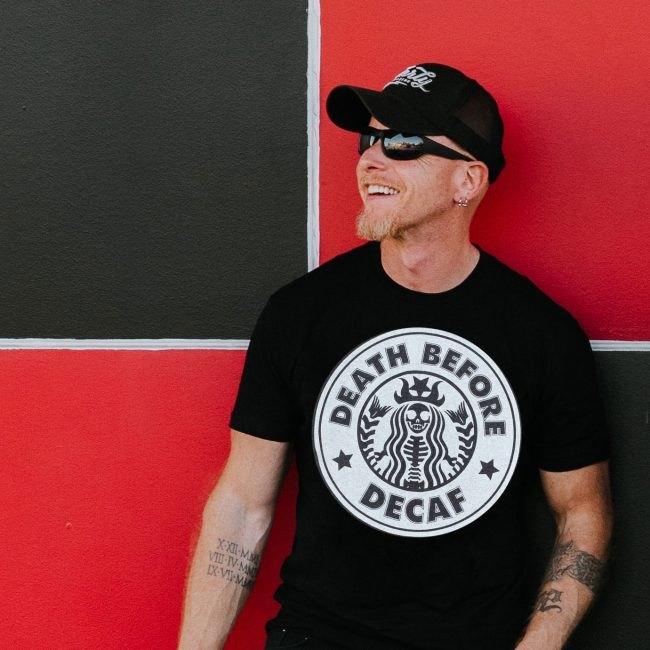 Jake Clark smiling in a cap and sunglasses against a red and black wall