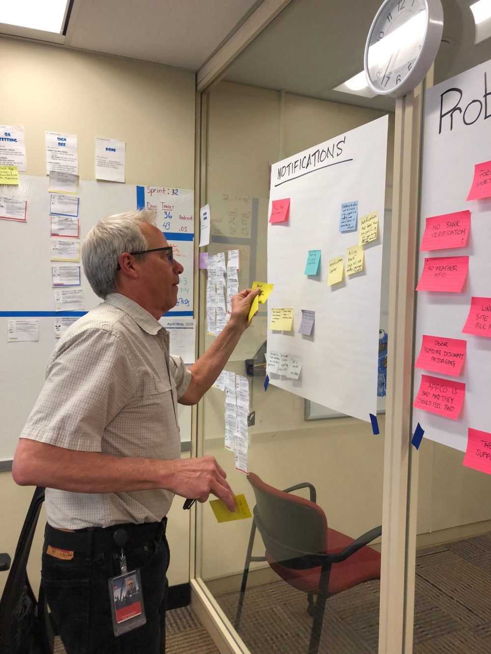 A team member adding sticky notes to a wall-sized notifications board